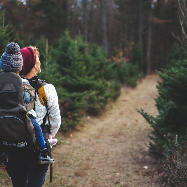 A woman carrying a child on her back in a forest, ensuring child protective measures are in place