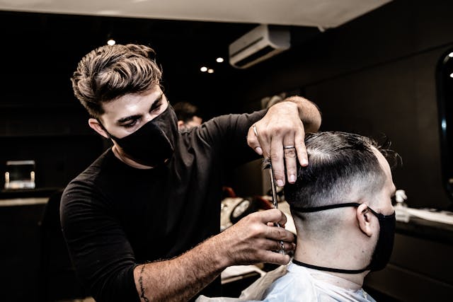 A man with a black face mask giving a haircut to another man. Hair Cutting License required